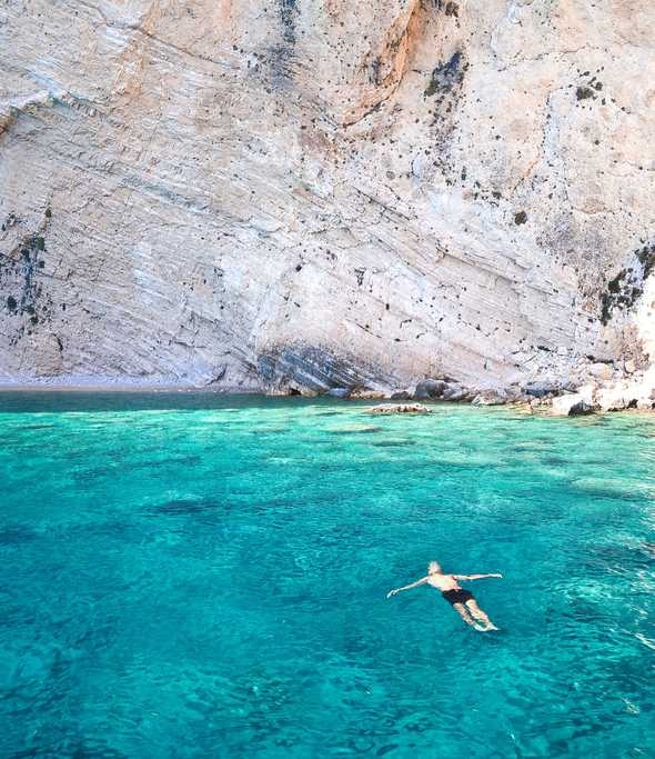 Man relaxing while floating on water near the rocks